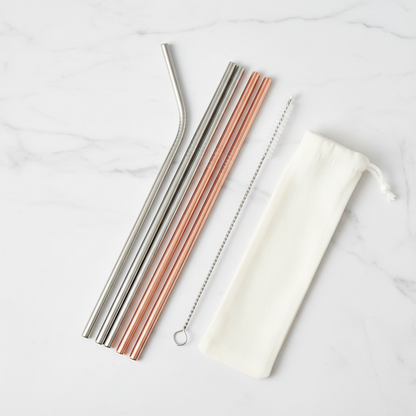 Set of reusable metal drinking straws in silver and rose gold with a cleaning brush on white marble
